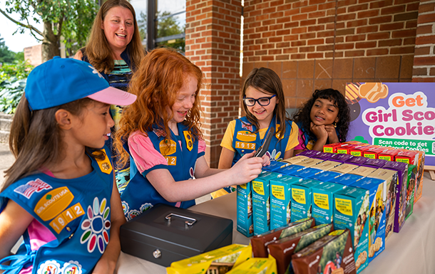 two adult volunteers with a group of girl scout daisies outside selling cookies